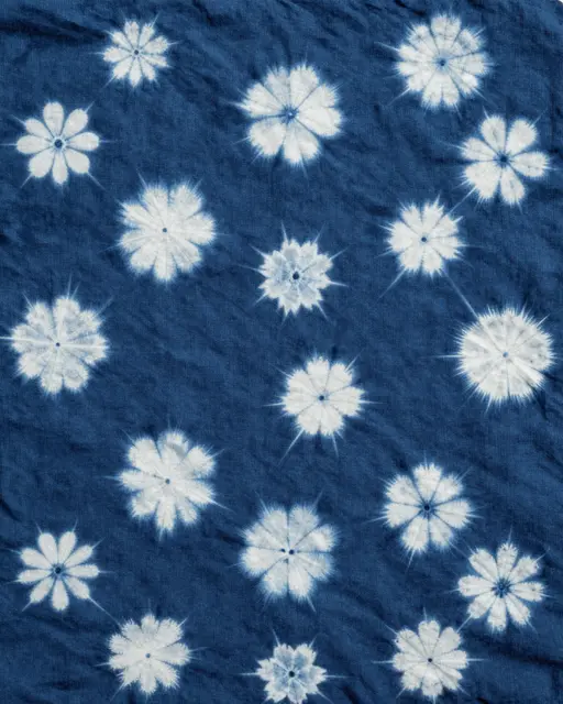 Full frame close-up of crinkled indigo cotton fabric with repeating white floral shibori tie-dye patterns under even flat