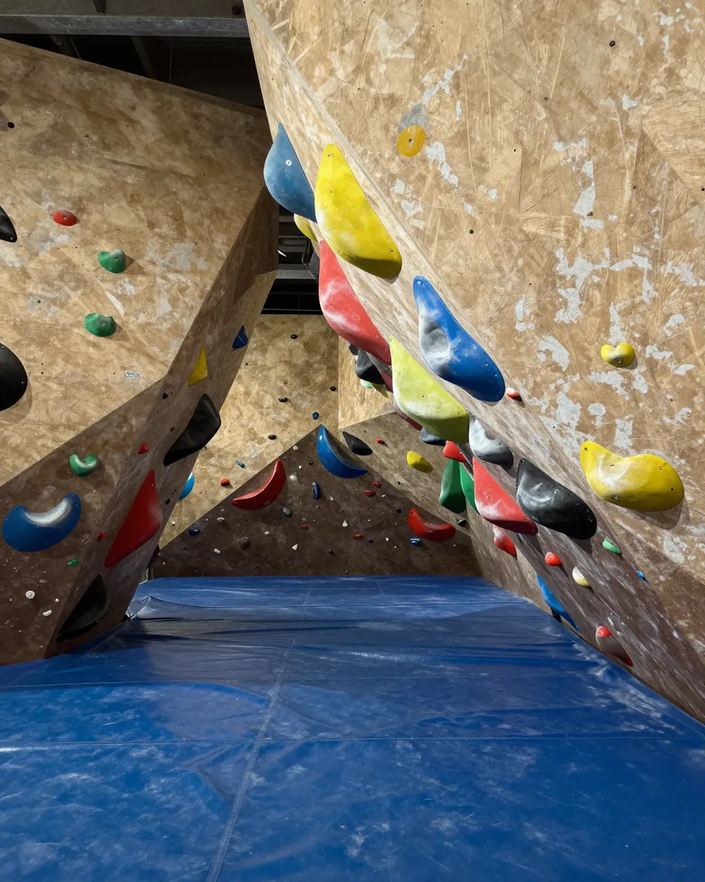 Empty indoor bouldering cave with colorful climbing holds and thick blue crash mat under overhanging walls