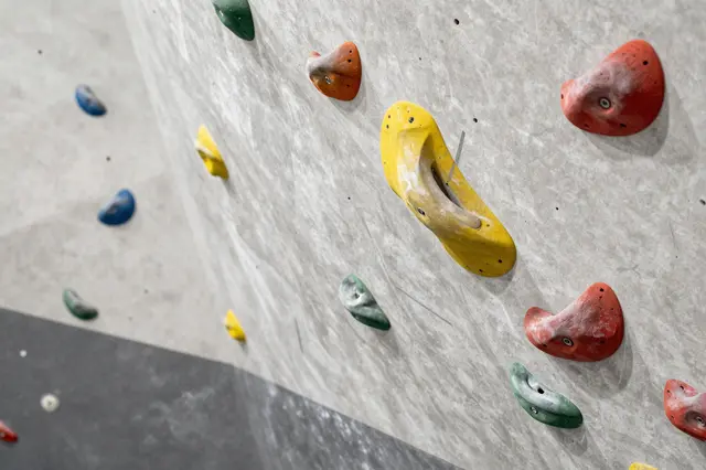 Textured indoor climbing wall fitted with multicolored plastic climbing holds.