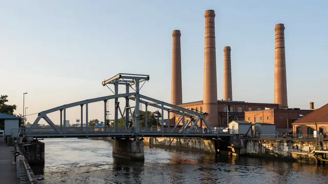 Riveted steel swing bridge spans an industrial canal beside tall brick chimneys at golden sunset