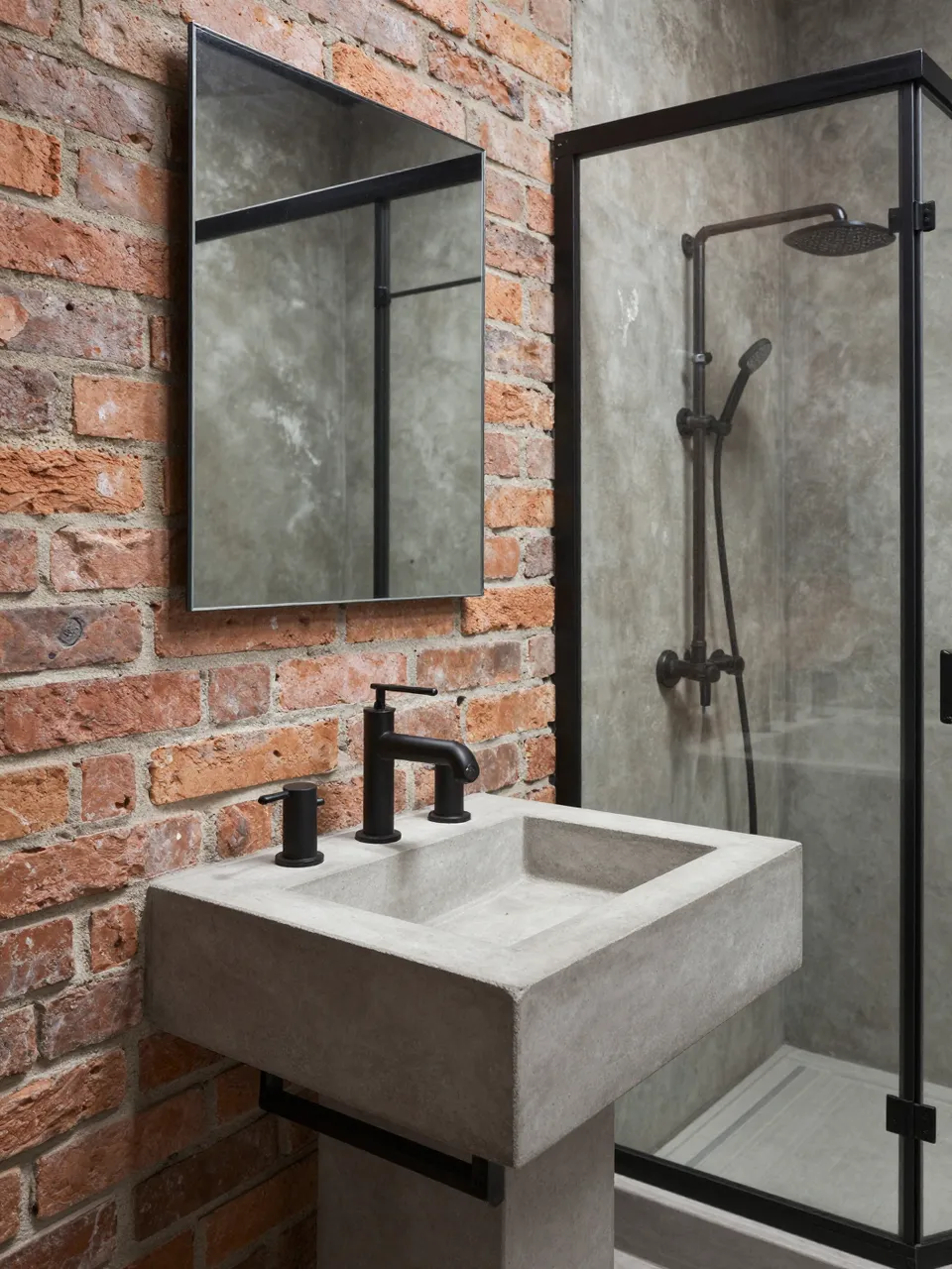 Modern industrial bathroom with exposed brick, concrete sink, and black framed glass shower enclosure