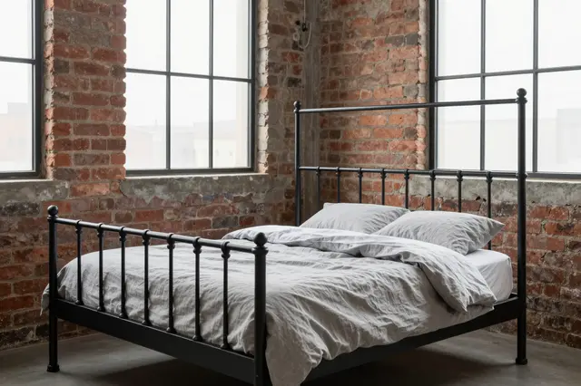Industrial loft bedroom with exposed brick, black iron bed and gray linen bedding under steel frame windows
