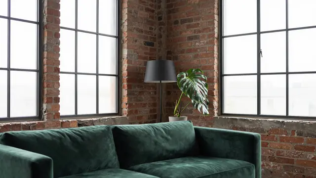 Unoccupied industrial loft corner with exposed brick, green velvet sofa, grid windows, floor lamp and potted monstera