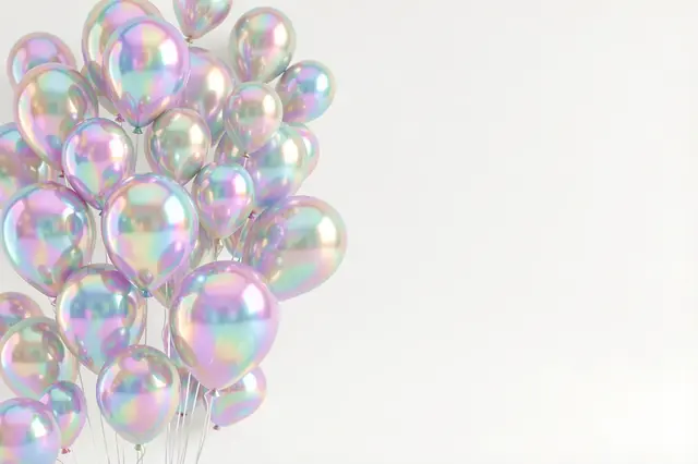 Cluster of holographic iridescent balloons sits on the left of a pearl white backdrop with empty copy space to the right