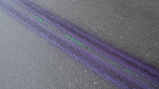 A streaked iridescent oil slick glows purple and green across dark wet asphalt pavement