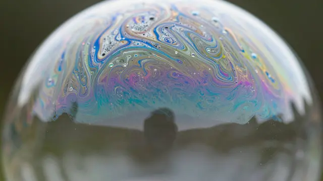 Close-up macro view of swirling iridescent color patterns across the curved surface of a soap bubble