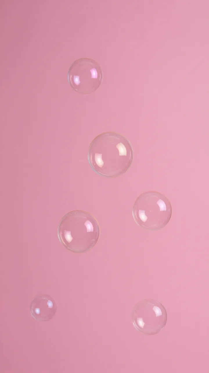 Clear floating soap bubbles rest against a solid hot pink studio backdrop.