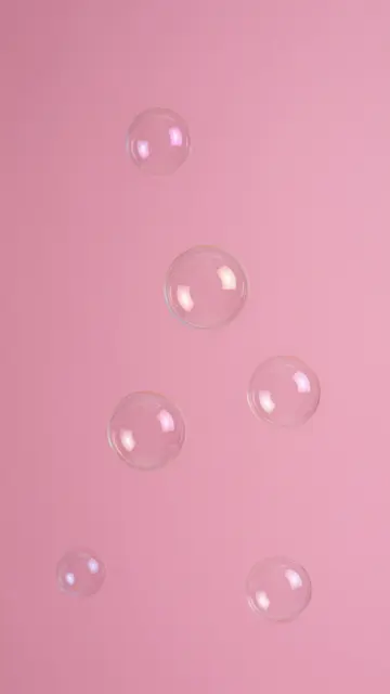 Clear floating soap bubbles rest against a solid hot pink studio backdrop.