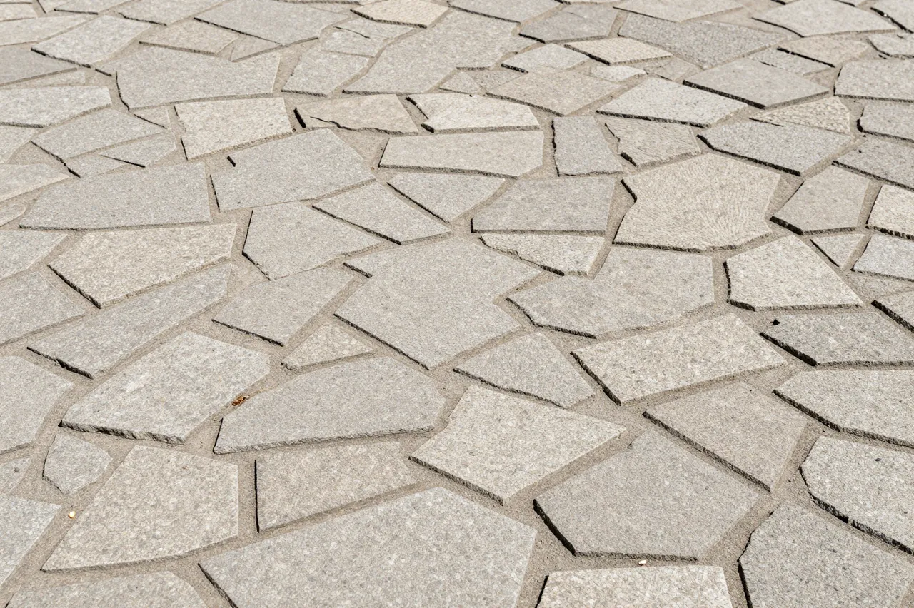 Full frame close-up of light gray irregular stamped flagstone concrete pavement in bright sunlight