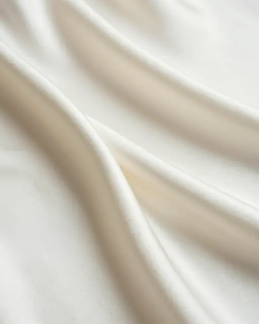 Softly lit close-up of draped ivory silk fabric with gentle curved ripples and empty copy space