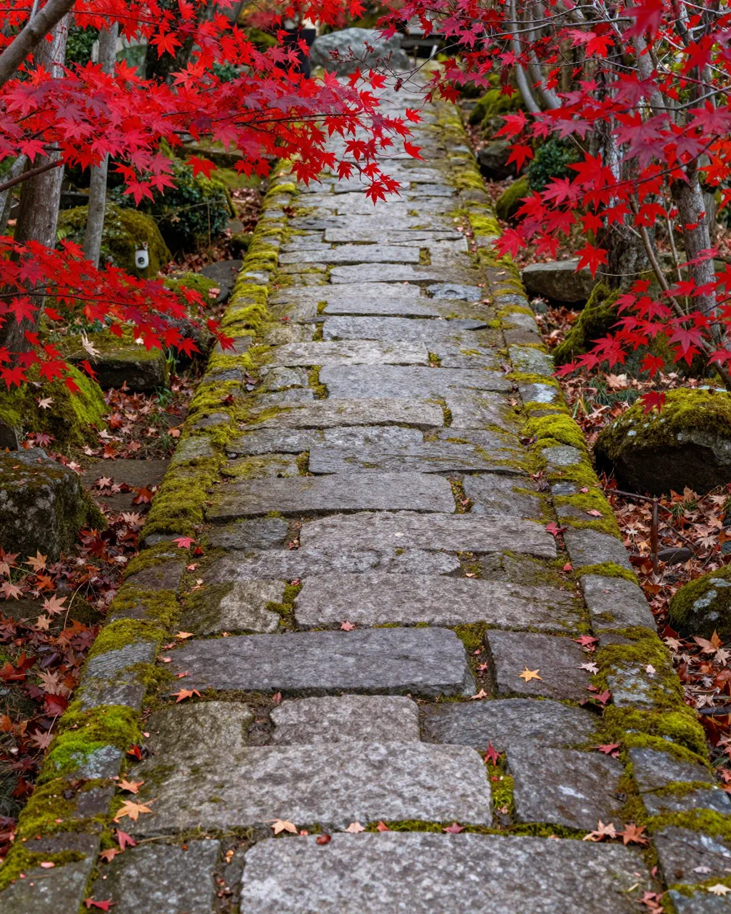 A moss-covered stone garden path lined with bright crimson maple leaves in autumn
