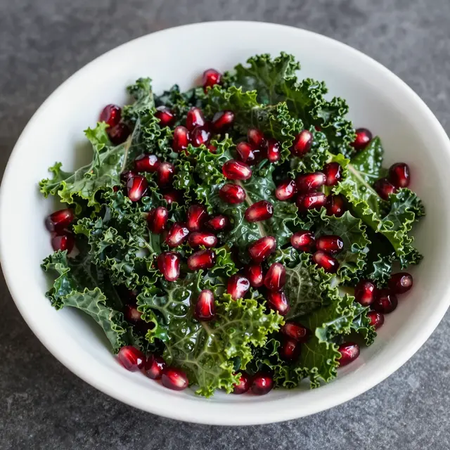 High angle view of a white bowl of fresh kale and pomegranate arils on a dark stone surface