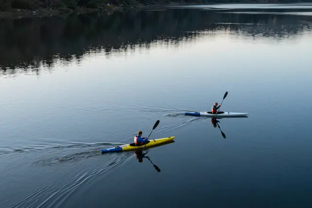 Aerial view of two kayakers paddling on a mirror-smooth calm lake at early dawn