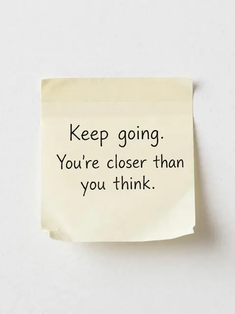 A cream sticky note on a white wall displays the text "Keep going. You're closer than you think." in black ink