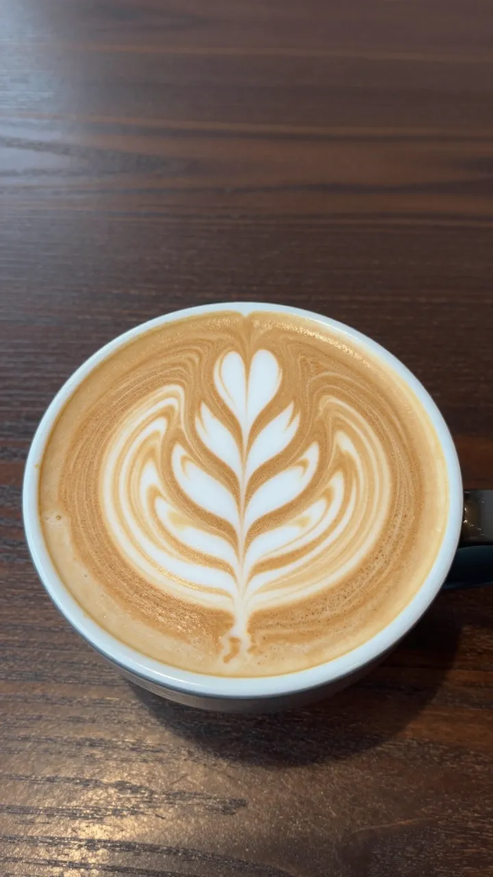 Top-down view of a latte with intricate leaf latte art resting on a dark wooden table