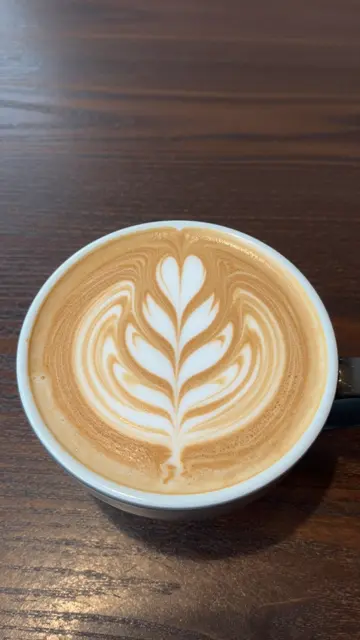 Top-down view of a latte with intricate leaf latte art resting on a dark wooden table