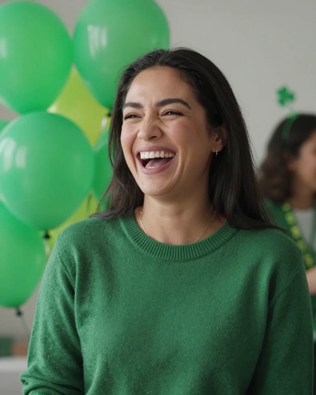A woman in a green sweater laughs heartily with green party balloons behind her