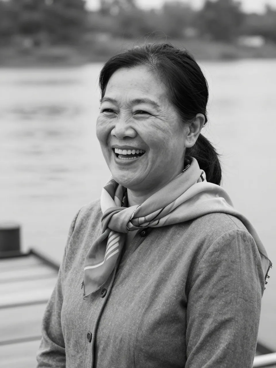 Black and white close-up portrait of a laughing mature Southeast Asian woman on a riverside dock