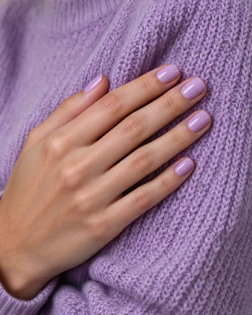 Close-up of a hand with glossy short round lavender nails resting on a soft lilac knit sweater