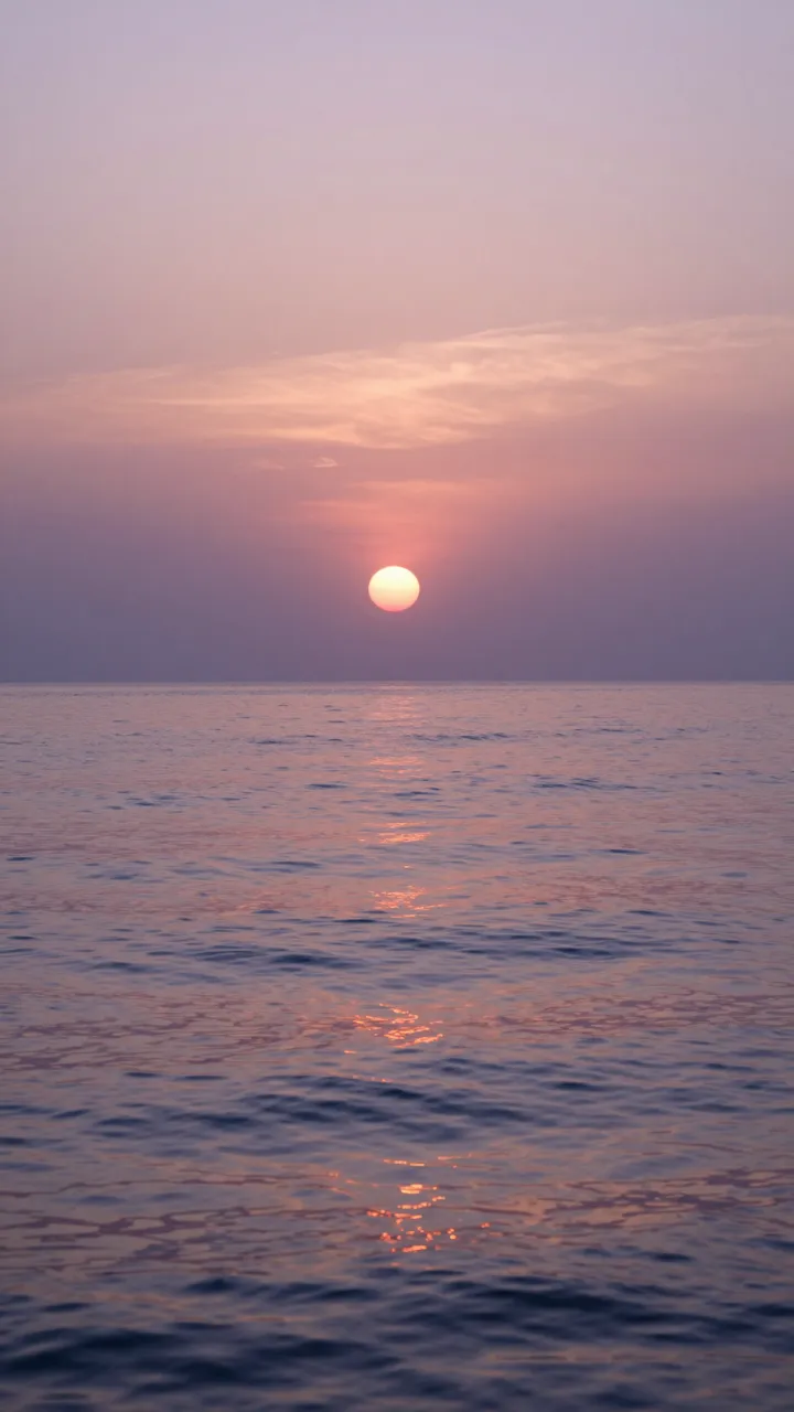Round sun hangs over a calm rippled sea beneath a soft lavender and peach sunset sky