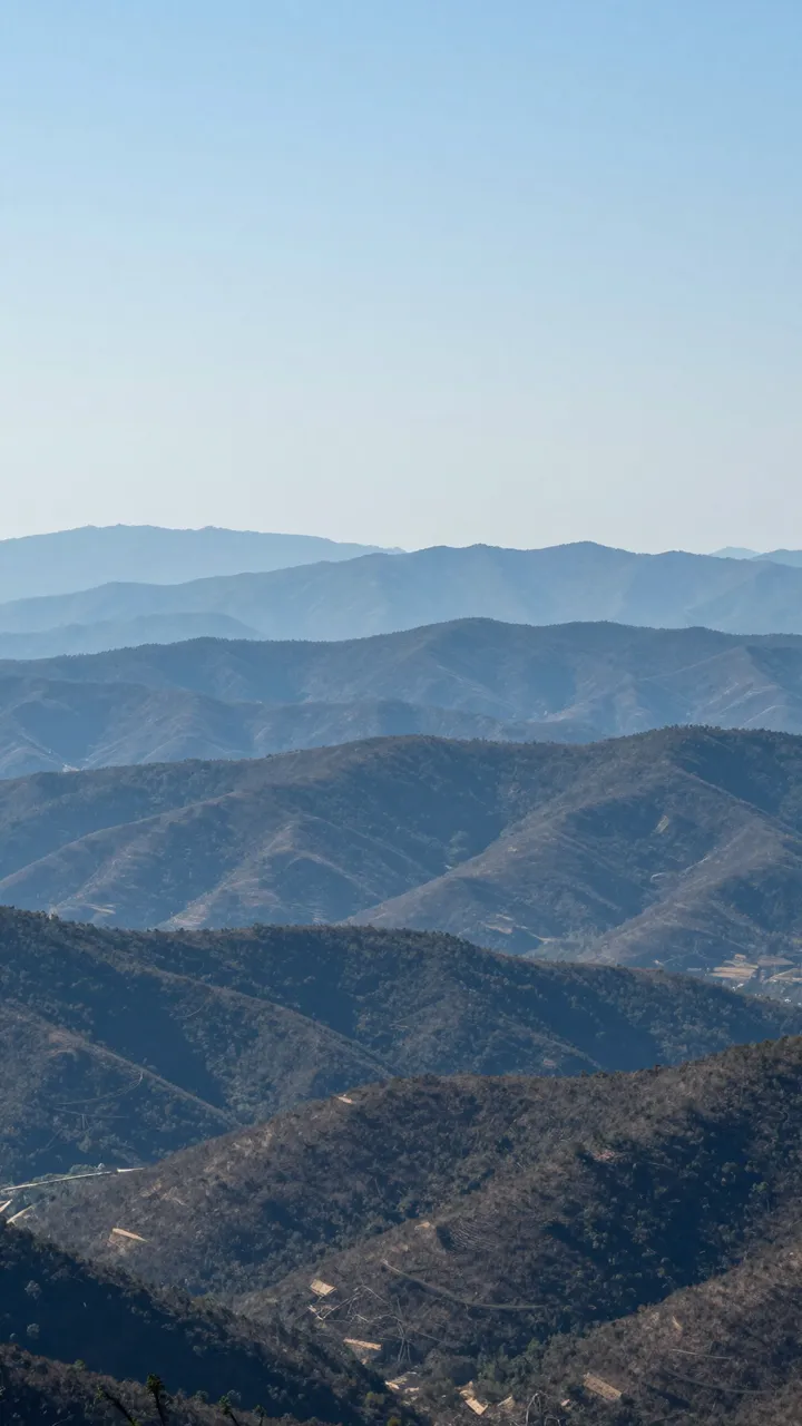 Vertical landscape of receding blue hazy mountain ridges under a clear pale blue sky with copy space