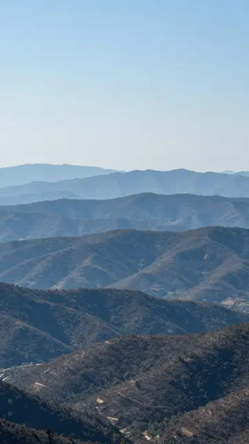 Vertical landscape of receding blue hazy mountain ridges under a clear pale blue sky with copy space