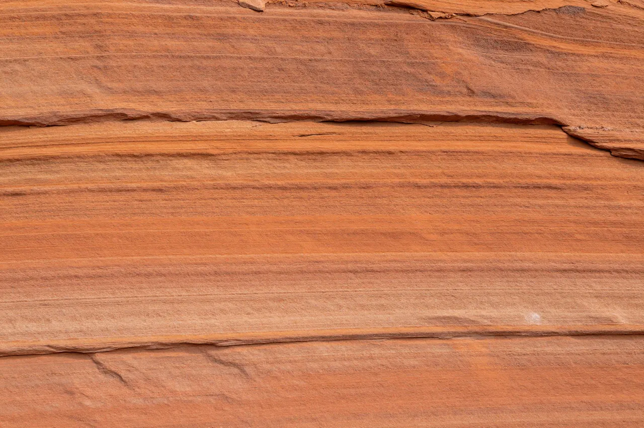 Full frame close-up of natural layered sandstone with warm orange horizontal bands and subtle cracks