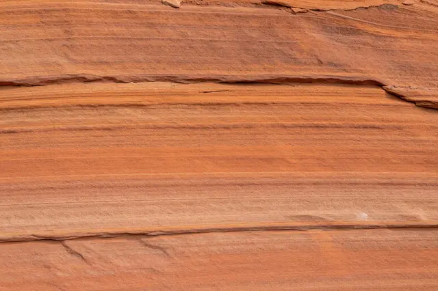 Full frame close-up of natural layered sandstone with warm orange horizontal bands and subtle cracks