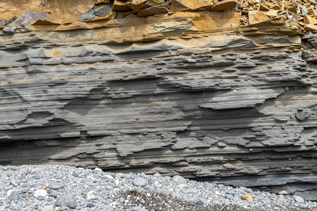 Eroded horizontal gray and ochre rock cliff rises above a pebble beach