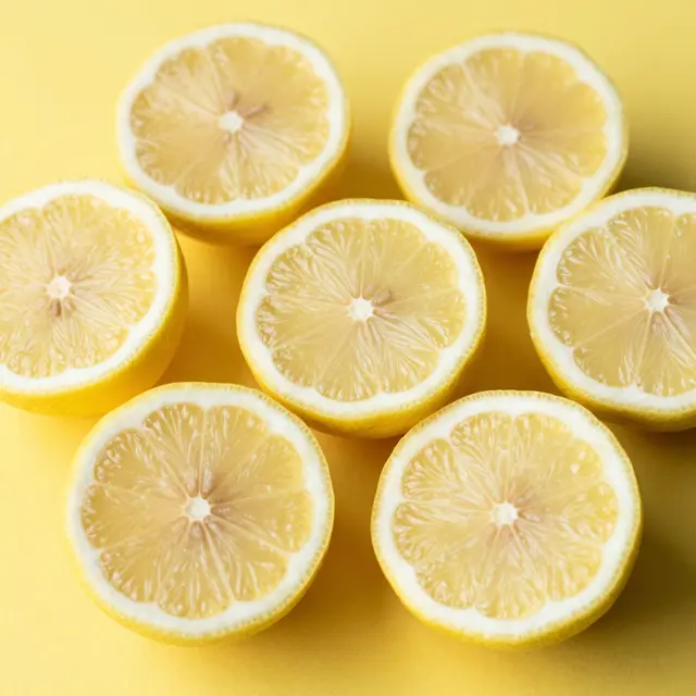 Top down view of seven fresh lemon halves arranged on a solid bright yellow background