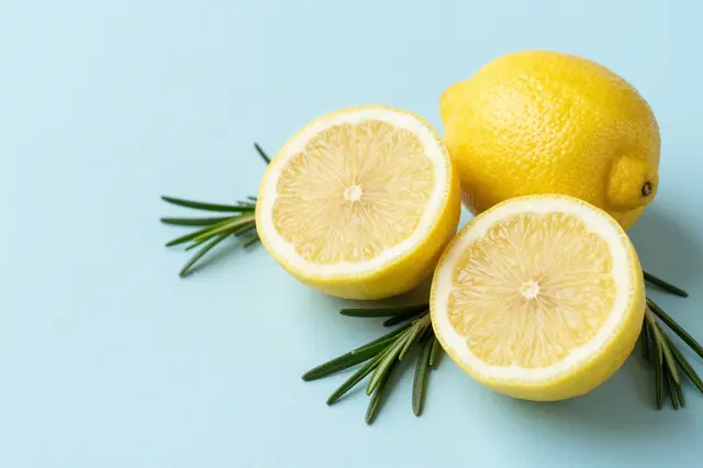 Whole and halved lemons with rosemary sprigs rest on a pale blue surface with empty left-side copy space