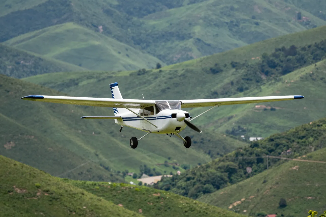 Small white and blue propeller plane flies low over rolling green mountain valleys