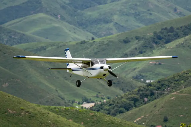 Small white and blue propeller plane flies low over rolling green mountain valleys