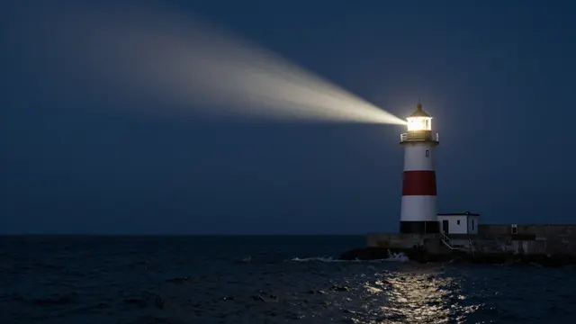 A red and white striped lighthouse casts a sweeping bright beam over dark ocean water at night