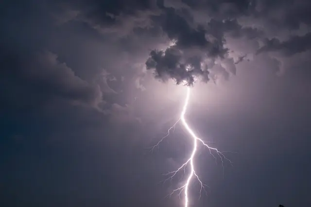 Bright jagged lightning bolt glows and bursts from dark roiling storm clouds at twilight