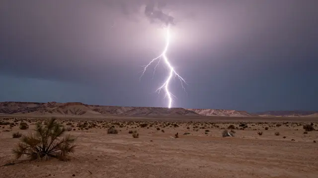 Bright lightning bolt strikes against a dark storm sky above an arid desert mesa landscape