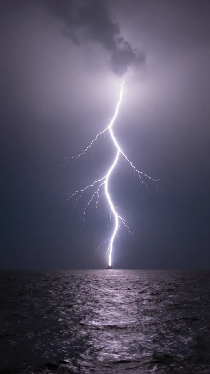 Bright jagged lightning strikes down through a stormy night sky over a dark rippled sea.