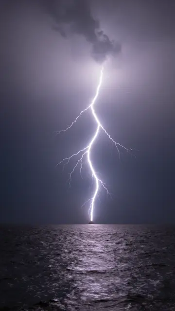 Bright jagged lightning strikes down through a stormy night sky over a dark rippled sea.
