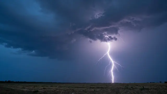 Bright lightning strikes across a dark stormy dusk sky above an open grassy plain