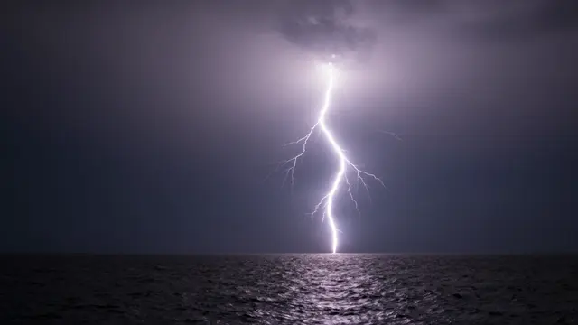 Bright vertical lightning bolt strikes the dark ocean surface beneath a stormy night sky