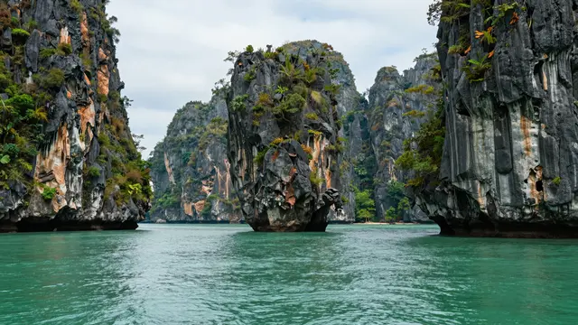 Towering limestone karst islands rise from calm emerald bay waters under an overcast sky