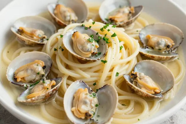 A close-up view of a bowl of linguine pasta with clams, fresh parsley, and creamy white wine sauce.