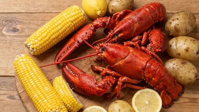 Overhead view of a cooked lobster boil spread with corn, potatoes and lemons on a wooden table
