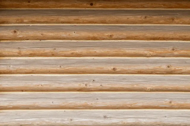Full frame close-up of horizontal round log cabin wall timbers with pale chinking lines between logs