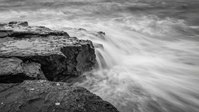 Black and white long exposure of misty ocean waves flowing over a rocky shore shelf