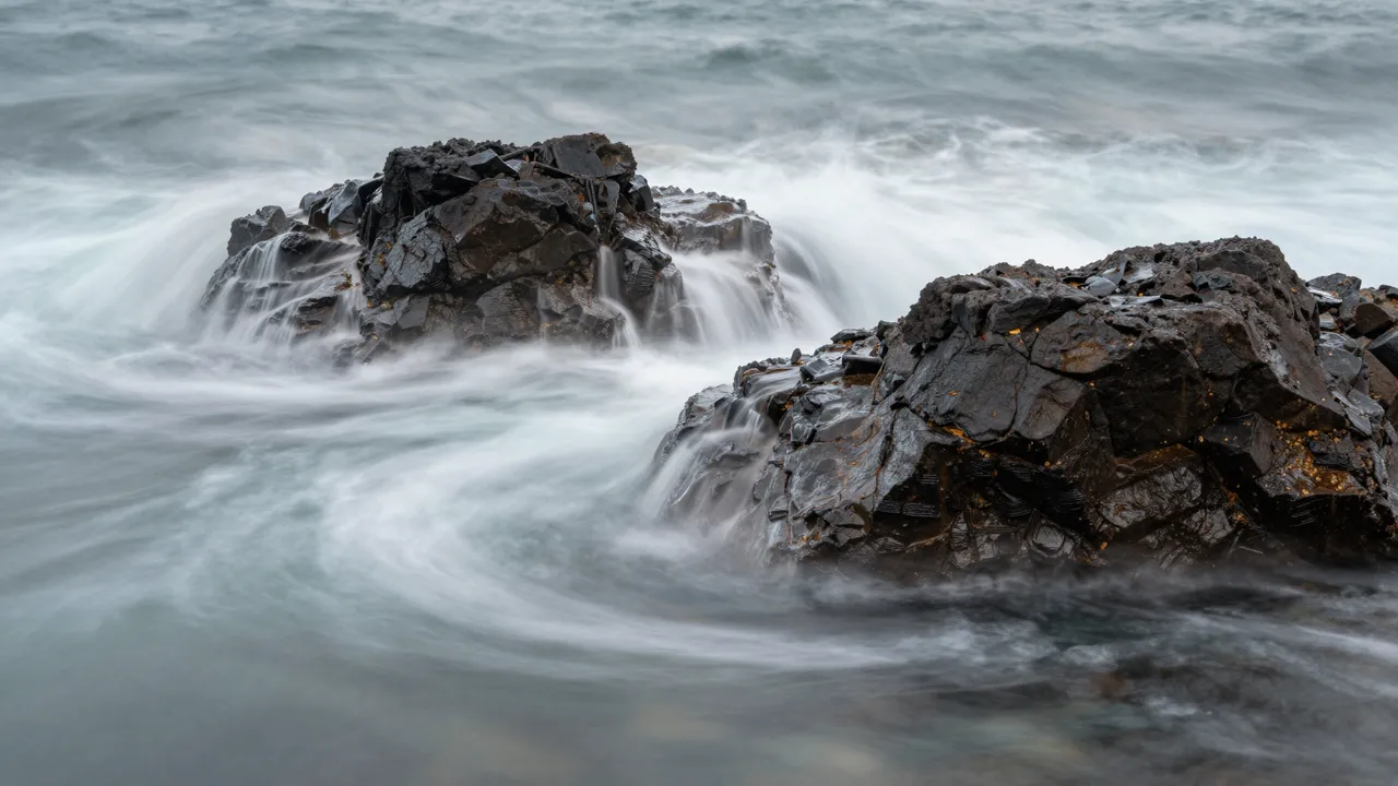 Silky blurred ocean waves flow around dark jagged coastal rocks in a long exposure shot