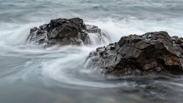Silky blurred ocean waves flow around dark jagged coastal rocks in a long exposure shot