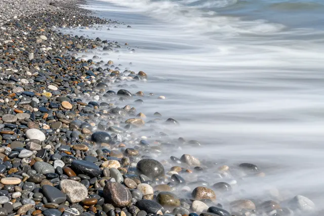 Smooth long exposure sea waves wash over multicolored smooth beach pebbles along a shoreline