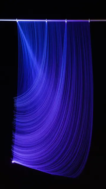 Wavy cobalt and violet light trails hang against a solid black background from a thin top rod
