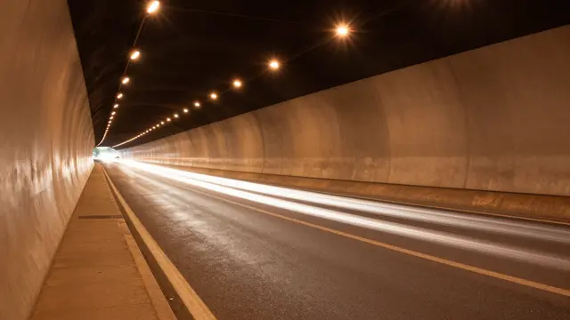 Curved concrete road tunnel with warm overhead lamps and bright traffic light streaks from passing vehicles